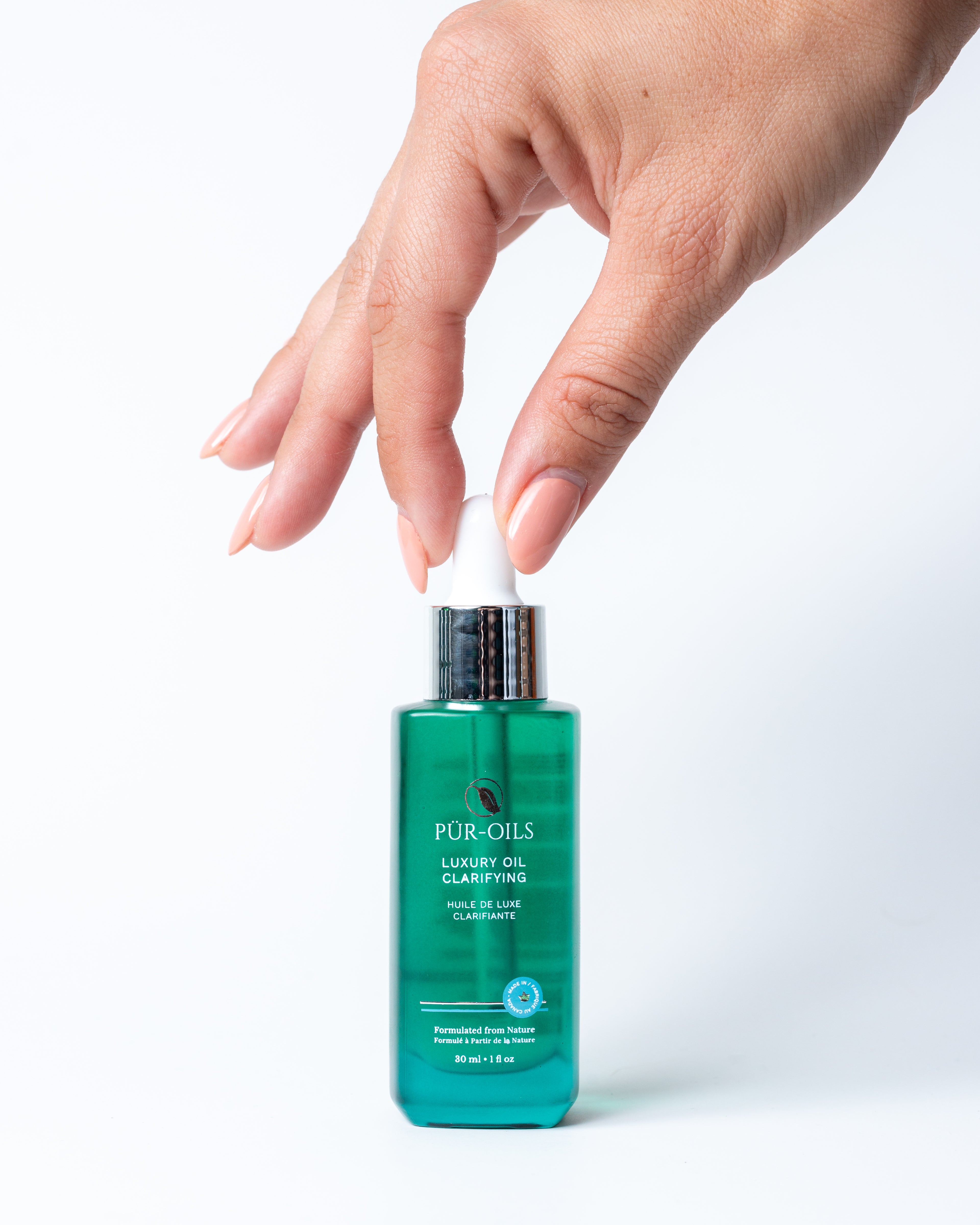 A person's hand reaching for a small bottle labeled 'Pür-Oils Clarifying' with a clear green liquid visible inside the bottle.