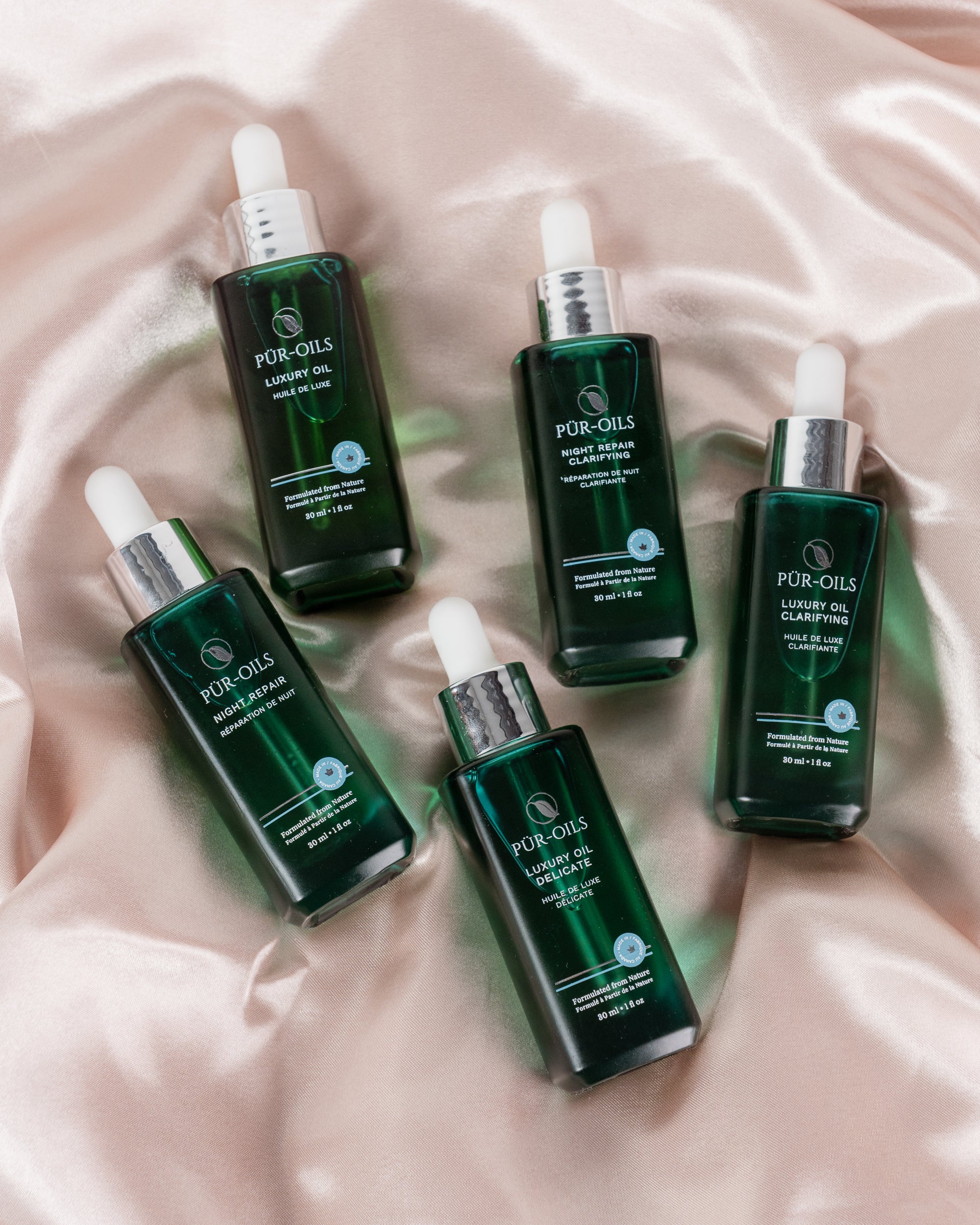 Five green skincare bottles with white caps on a soft pink fabric background